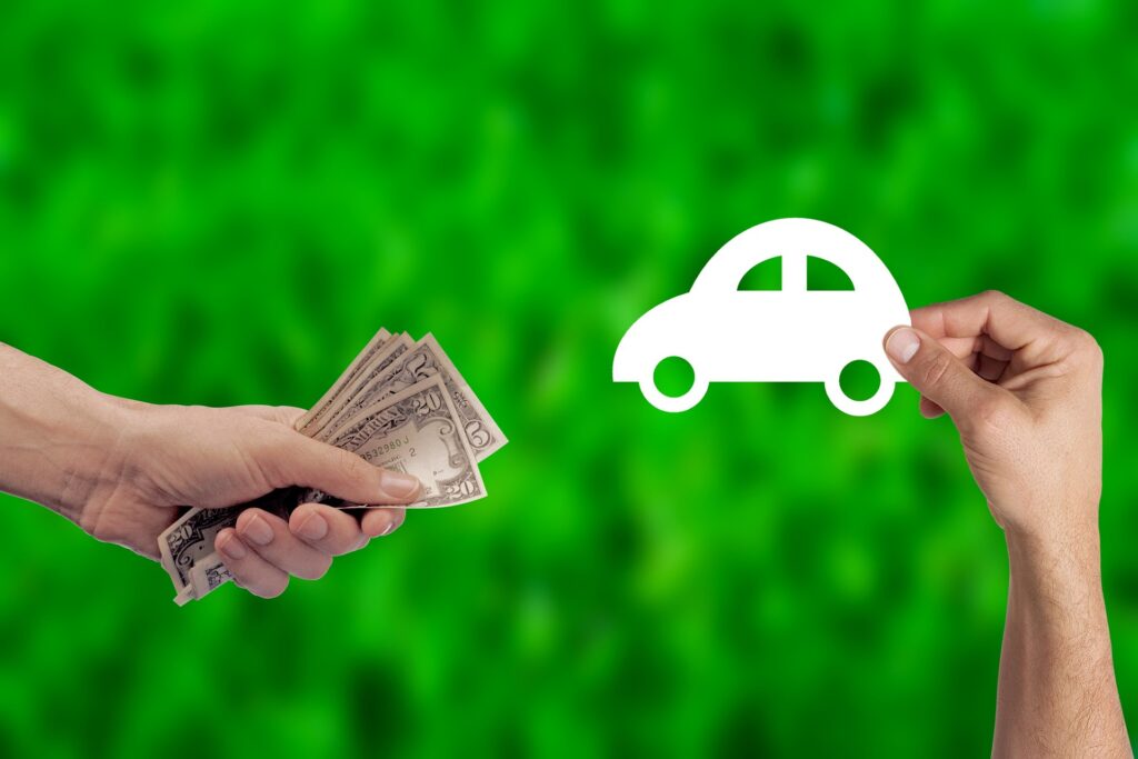 Hur fungerar bilförsäkring vid ägarbyte?  bild på en hand som håller sedlar medan handen bredvid håller i en pappersbit som är utklippt som en bil.